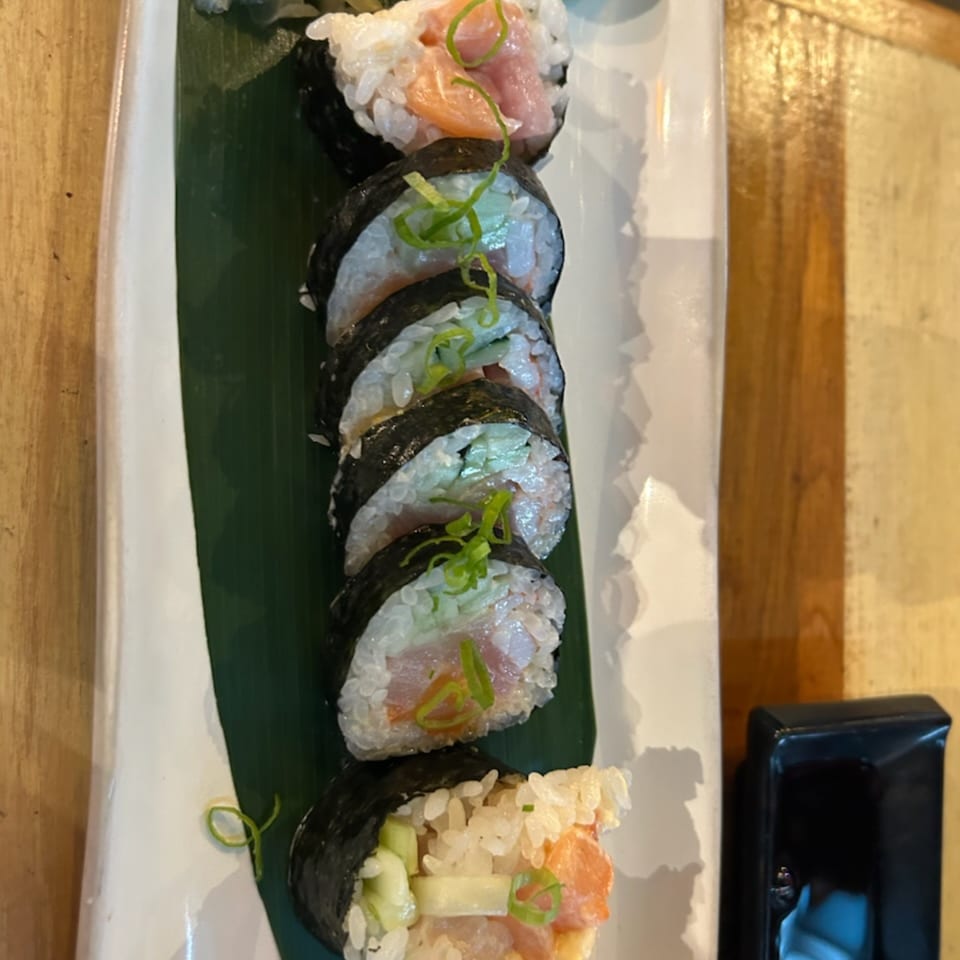 A row of Bistro Saffron's Asian-fusion sushi rolls with salmon, tuna, and cucumber on a white plate.