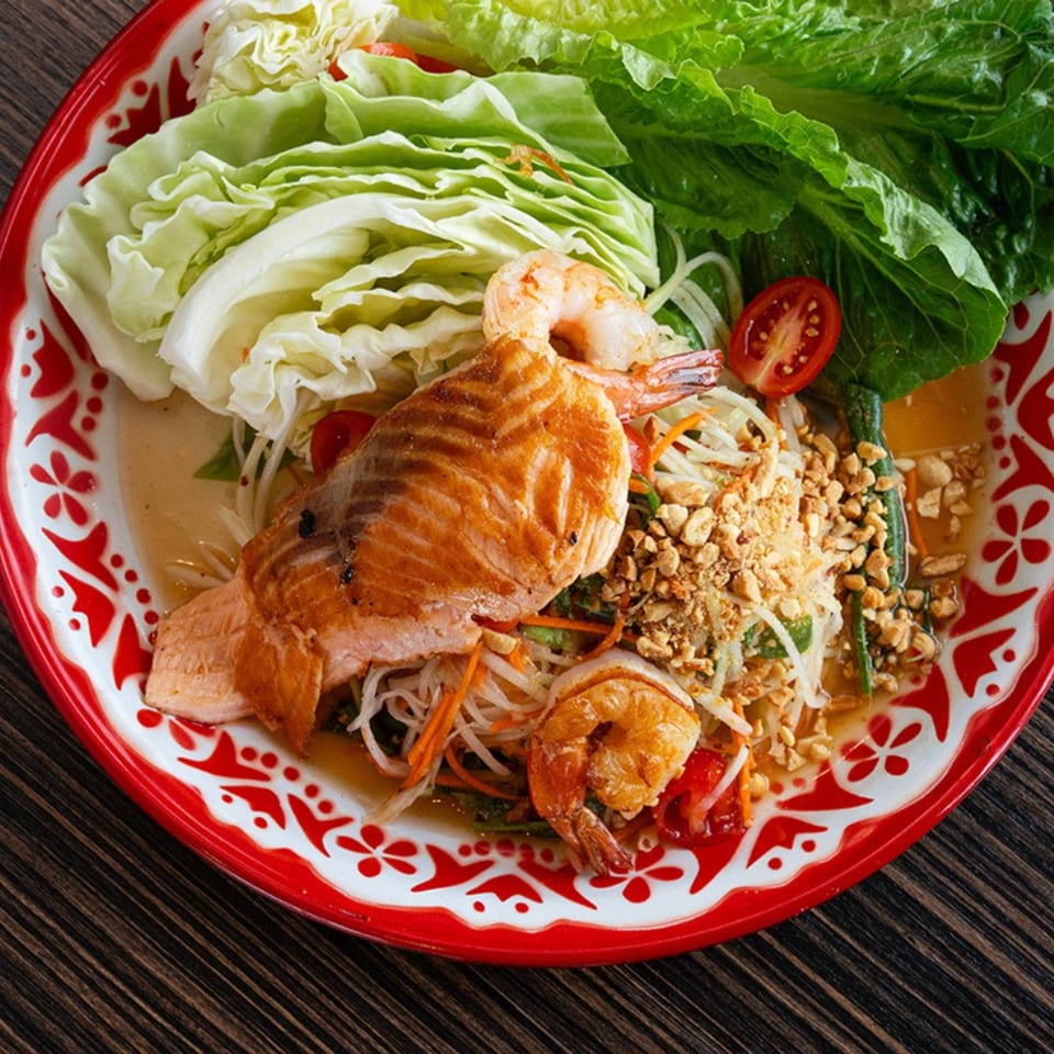 Bistro Saffron's Asian-fusion dish with grilled salmon, shrimp, salad, and peanuts on a red and white plate.