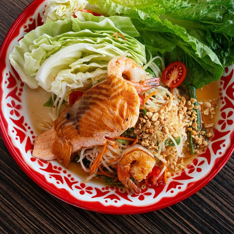 Bistro Saffron's Asian-fusion dish with grilled salmon, shrimp, salad, and peanuts on a red and white plate.