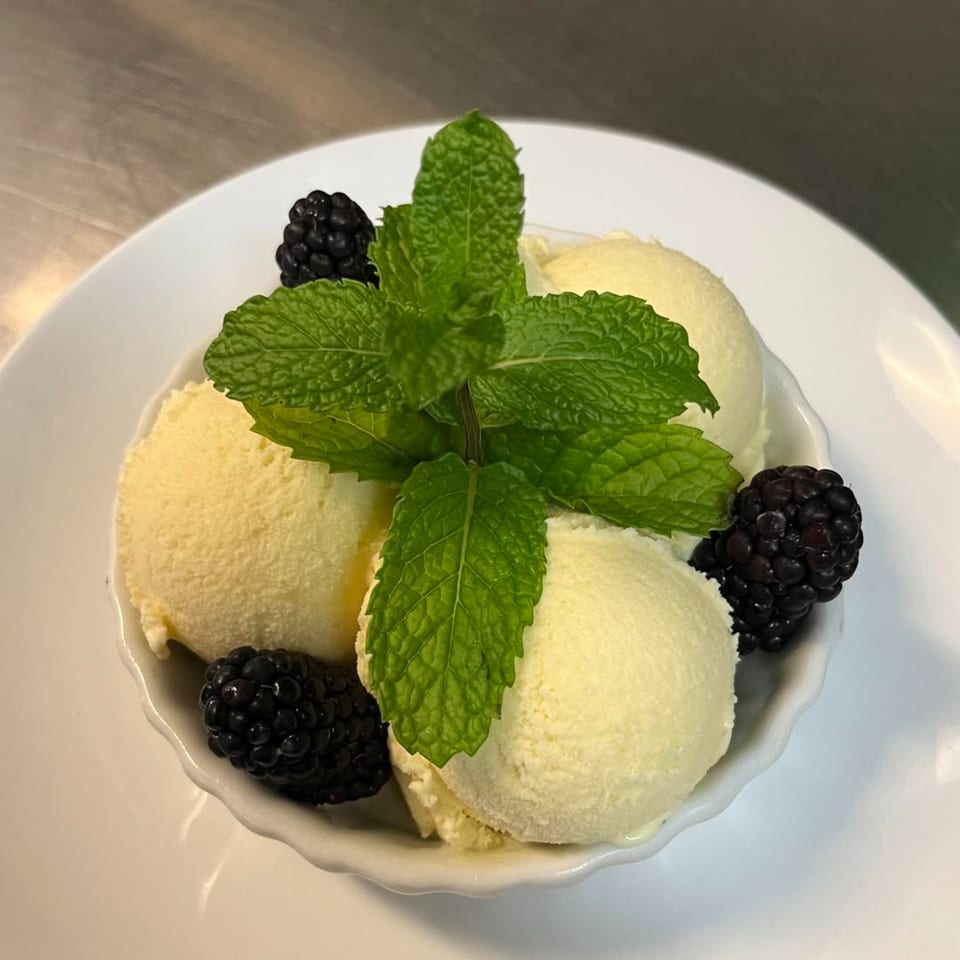 Scoops of light yellow ice cream in a white bowl, garnished with fresh mint and blackberries.
