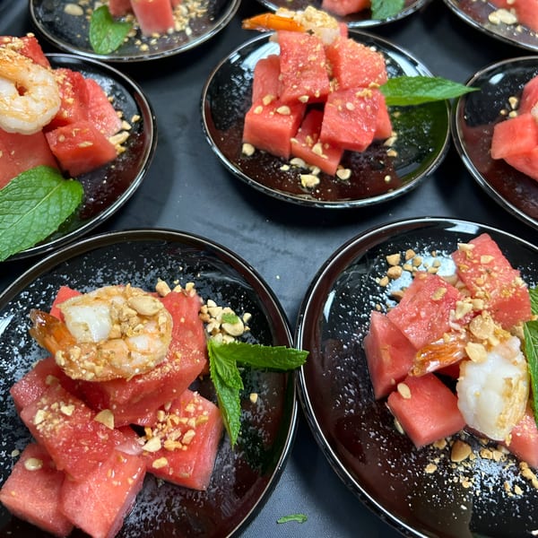Several small plates of watermelon cubes topped with shrimp, crushed peanuts, and mint leaves.