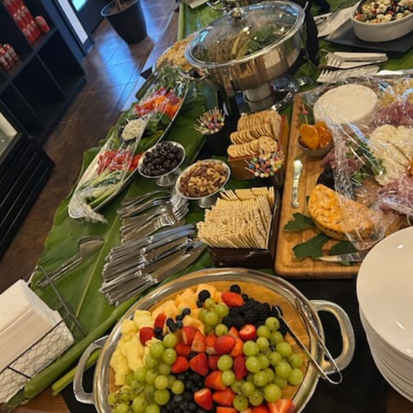 An Asian-fusion buffet spread with fruit, crackers, cheeses, and hot dishes on a banana leaf runner.