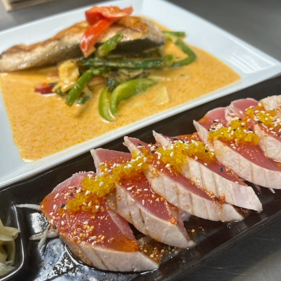 Seared tuna sashimi with roe and sesame seeds, alongside fish in yellow curry with vegetables.